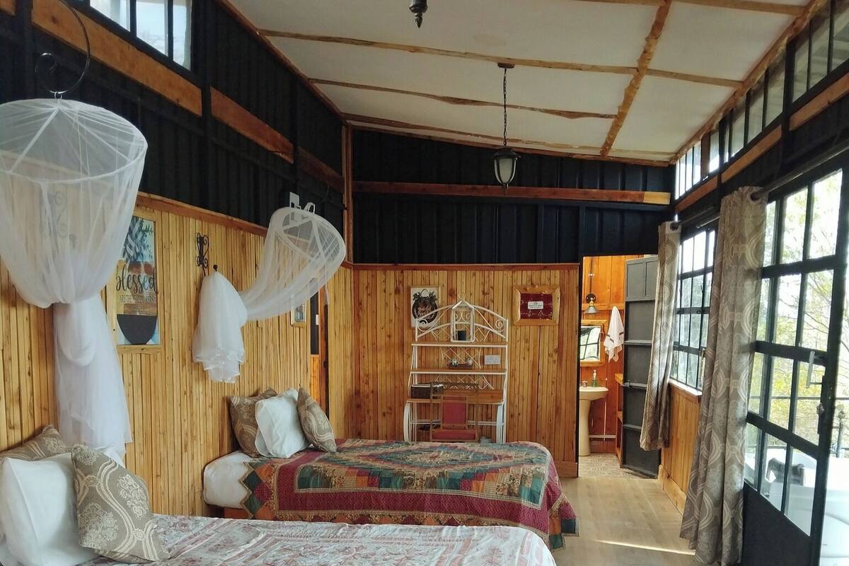 Ein Zimmer mit zwei Betten, Holzwänden, einem großen Fenster und einer hängenden Leuchte.