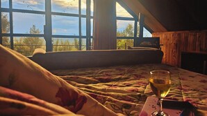 A bedroom with a large window, a bed with floral bedding, and a glass of wine on the nightstand.