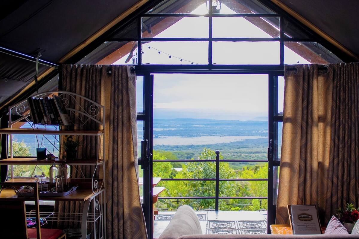 Ein gemütliches Zimmer mit großem Fenster und schöner Aussicht auf ein Tal.