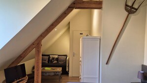 A bedroom with a sloped ceiling, a bed, a television on a small table, a wooden floor, and a door.