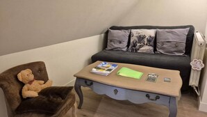A cozy room with a brown leather chair, a small wooden table with magazines, and a grey sofa with patterned cushions.