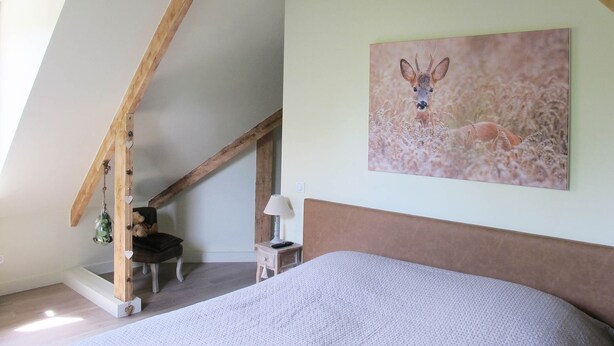 A bedroom with a sloped ceiling, a bed, a chair, a small table, and a wall-mounted picture of a deer. - Quiet Chambre des Daims (BERTHEN)