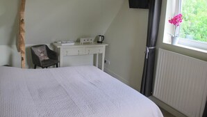A bedroom with a bed, a small desk with a kettle, a chair, a window with a plant, and a radiator. - Quiet Chambre des Daims (BERTHEN)