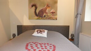 A bedroom with a bed, a pillow with a squirrel design, a heart-shaped decoration on the bedspread, and a painting of a squirrel on the wall.