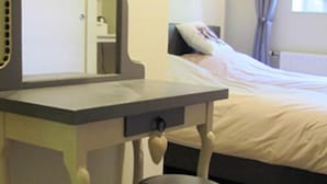 A bedroom with a bed, a bedside table with a mirror, and a window with curtains.