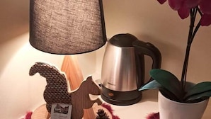 A table with a lamp, a coffee maker, a potted plant, a decorative wooden horse, a sign, and a tray with a cake and a spoon.