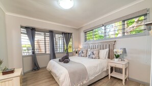 A bedroom with a large bed, a bedside table with a lamp, and a window with curtains.
