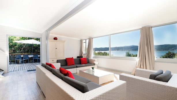 A modern living room with a large window, a sofa set, and a dining area with outdoor seating.