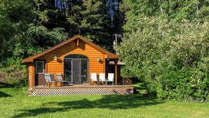 A wooden cabin with a porch, two chairs, and a large window.