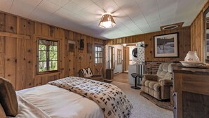 A cozy room with a large bed, wooden walls, a fireplace, and a dining area.