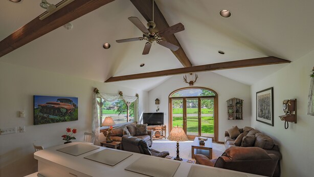 A spacious living room with a high ceiling, a ceiling fan, and a large window offering a view of a green landscape.