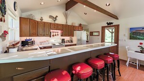 A kitchen with wooden cabinets, a large island with stools, and a dining area with a white table and chairs.