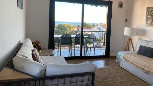 A room with a bed, a sofa, a dining table, and a view of the ocean through a large sliding door. - Bright apartment with sea view (Calafell)