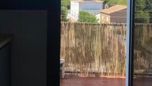 A view from a room with a large window, a wooden door, and a balcony with a fence. - Bright apartment with sea view (Calafell)