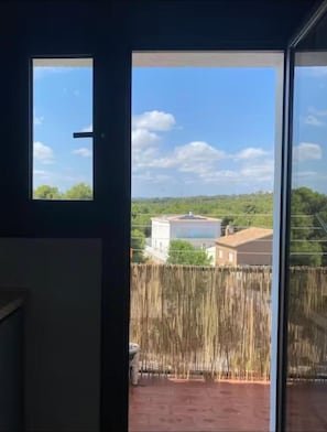 Vista desde una habitación con un ventanal, una puerta de madera y un balcón con barandilla.