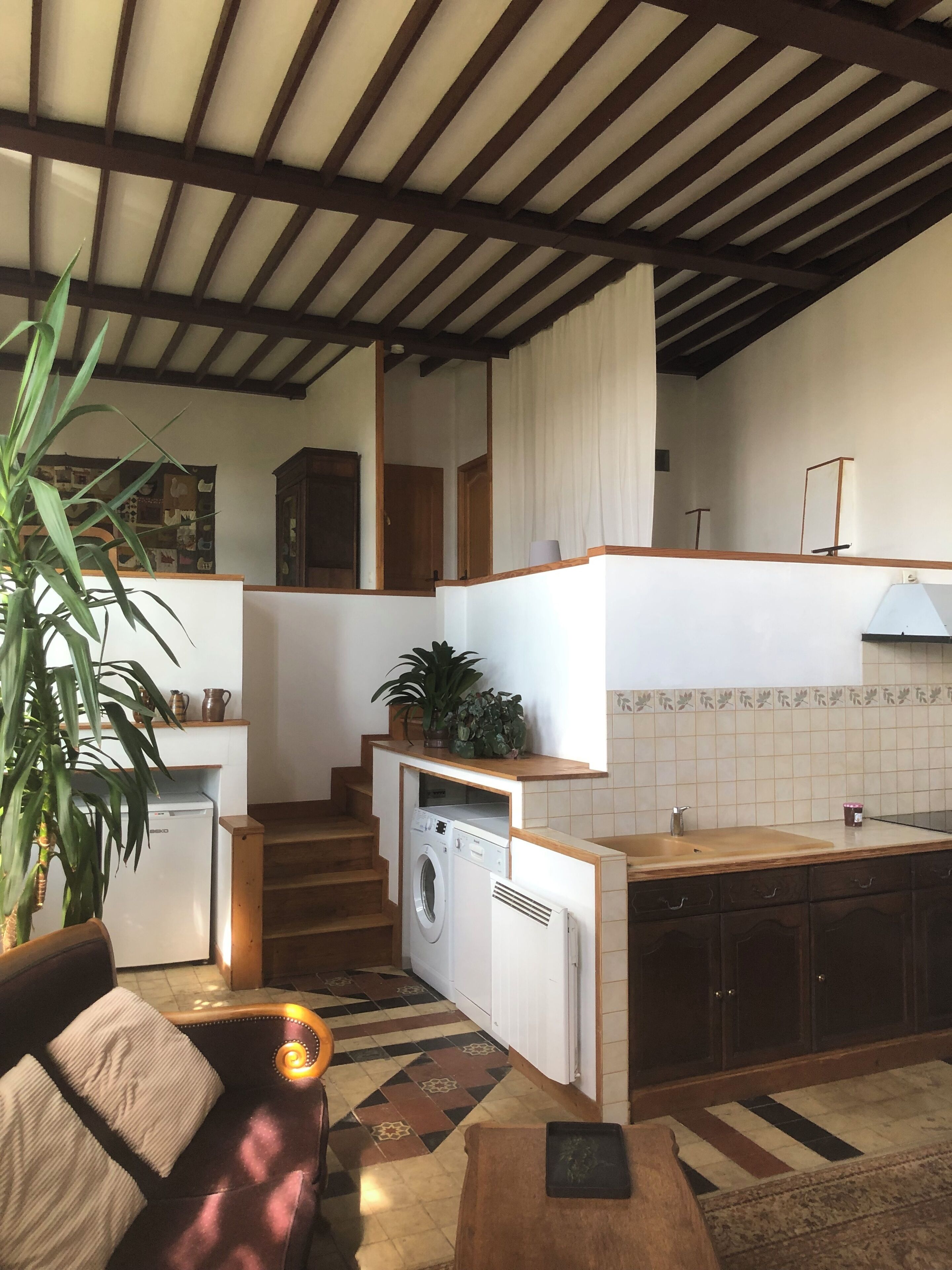 A compact living space with a kitchen, a washing machine, a dining area with a sofa, and a staircase.