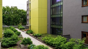 A modern building with a green facade, a narrow pathway, and lush greenery.