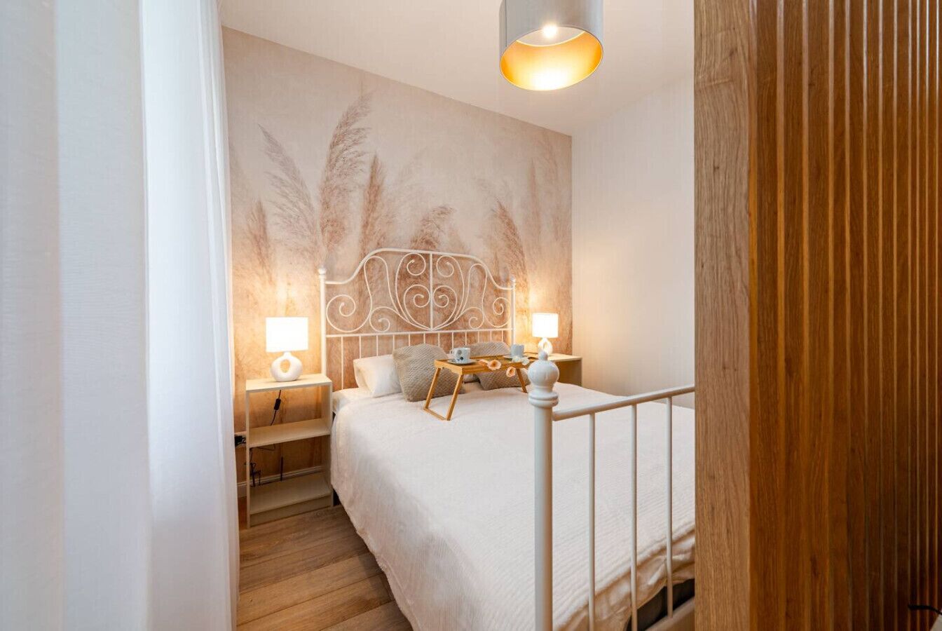 Un dormitorio con cama, mesitas de noche, lámpara de pared y suelo de madera.