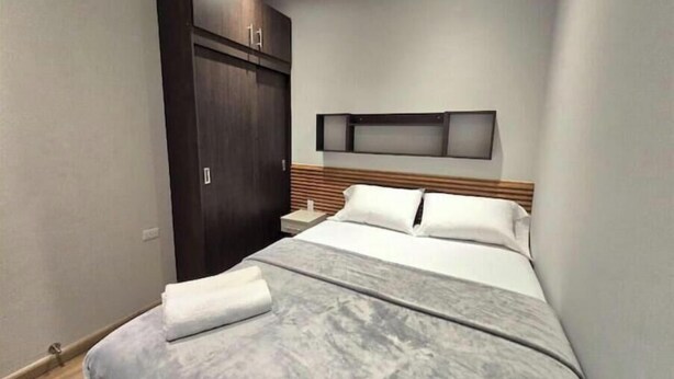 Una habitación de hotel moderna con una cama grande, un armario de madera y un televisor montado.