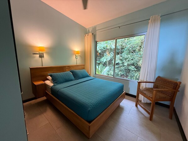 A bedroom with a bed, two bedside lamps, a window with curtains, and a chair.