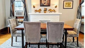 Une salle à manger avec une cheminée blanche, deux fauteuils et une table.