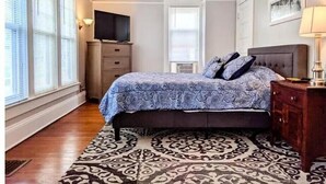 Une chambre à coucher comprenant un lit, un ventilateur de plafond, une commode, un téléviseur et un tapis à motifs.