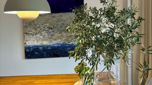 A room with a wooden floor, a modern pendant light, a large abstract painting, and a potted plant.