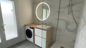 A modern bathroom with a glass-enclosed shower, a built-in washing machine, and a vanity with a mirror.