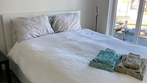 Ein Schlafzimmer mit einem großen Bett, einem Nachttisch und Blick ins Freie durch ein Fenster.