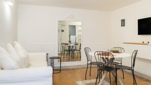 A modern living room with a white sofa, a dining table with chairs, a flat-screen TV mounted on the wall, and a mirror reflecting the dining area. - Secret House by Wonderful Italy (Bari)