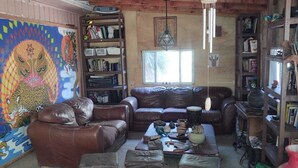 A rustic living room with a brown leather sofa, a wooden coffee table, and a bookshelf filled with books and decorative items. - HOUSE OF ANCESTRAL MEDICINES AND MASTER PLANTS (tijuana)