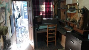 A small, rustic room with a wooden desk, a chair, a lamp, and a window with a plaid curtain. - HOUSE OF ANCESTRAL MEDICINES AND MASTER PLANTS (tijuana)