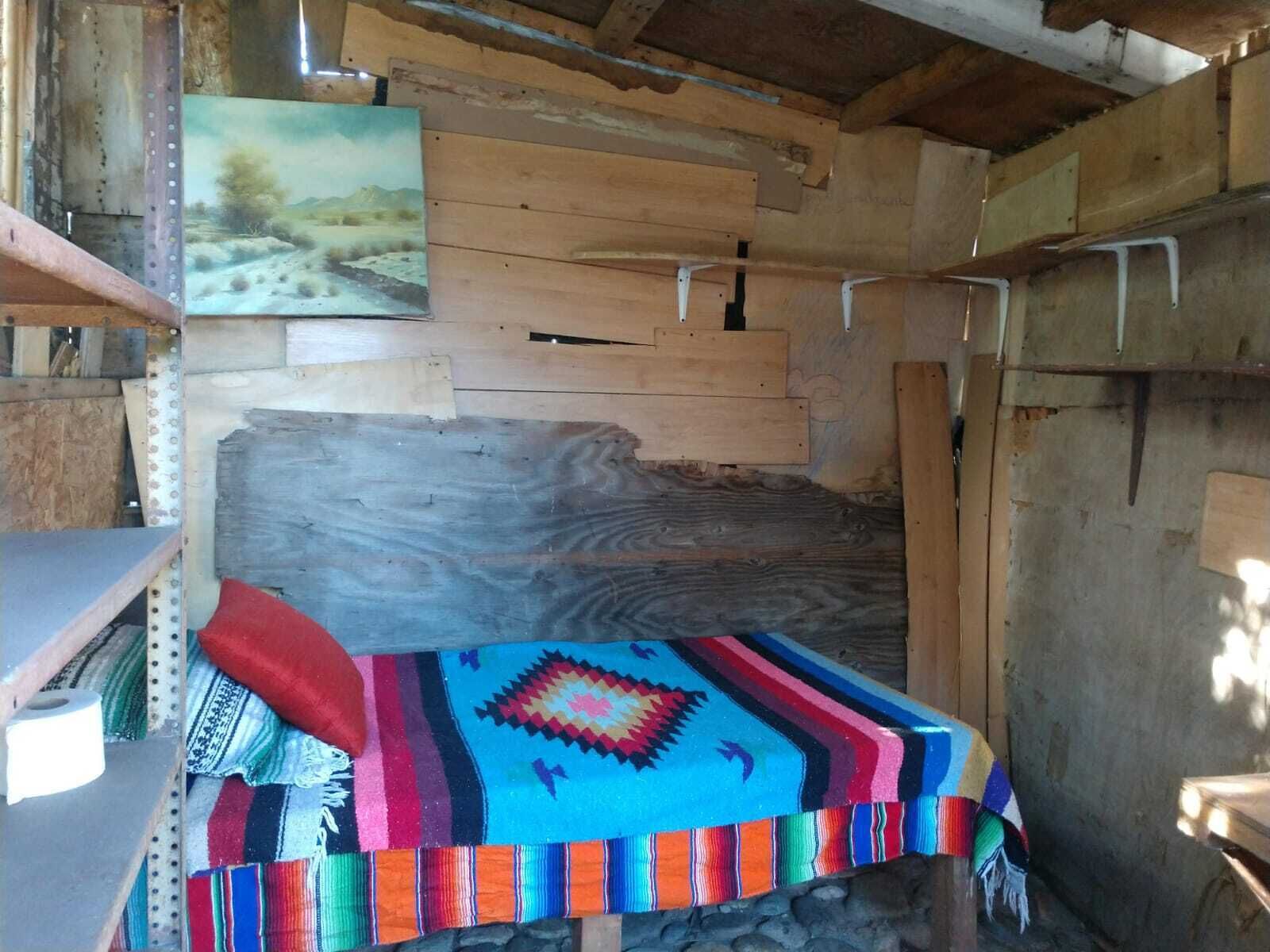 A rustic room with a wooden bed, a colorful blanket, and a painting on the wall.
