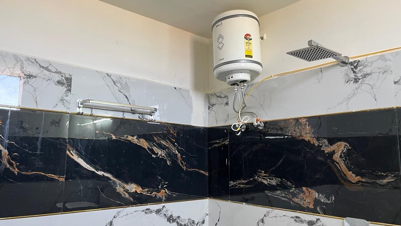 Un baño con baldosas de mármol blanco y negro, un calentador de agua blanco y un cabezal de ducha.