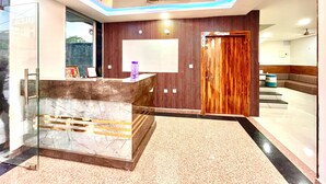 A modern reception area with a marble reception desk, wooden panel walls, and a reception desk with a framed picture and a purple bottle. - manya palace (Orchha)