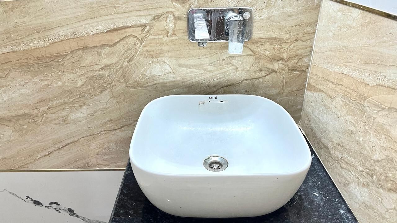 A bathroom with a white sink, marble walls, and a black countertop.