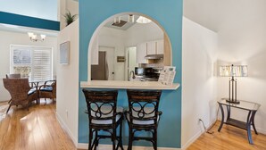 A modern kitchen with a blue accent wall, a dining area with wicker chairs, and a small table with a lamp.