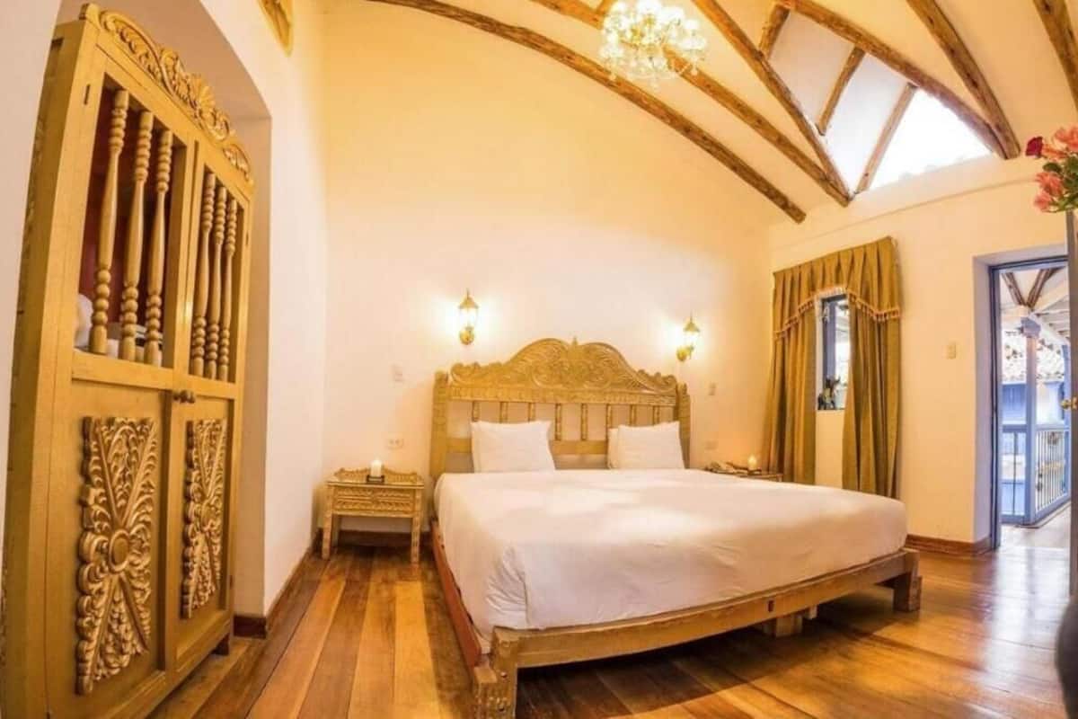 A bedroom with a wooden bed, a nightstand, a chandelier, and a large window with curtains.