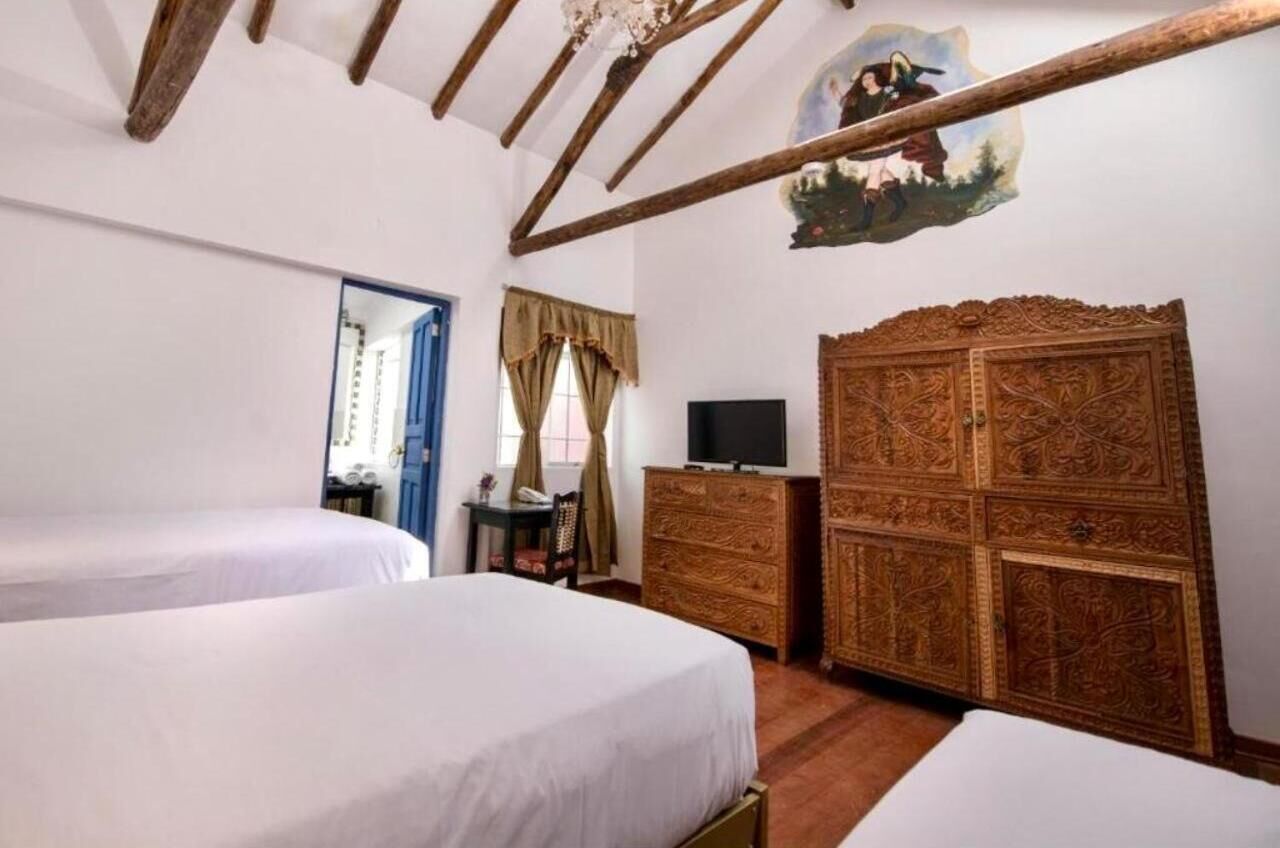 A bedroom with two beds, a wooden wardrobe, a television, and a painting on the wall.