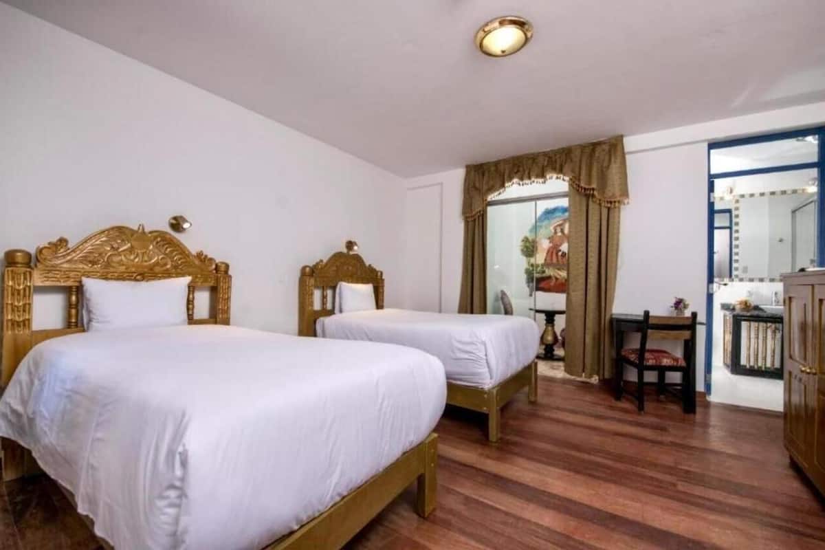A room with two wooden beds, a small table with a chair, and a mirror on the wall.