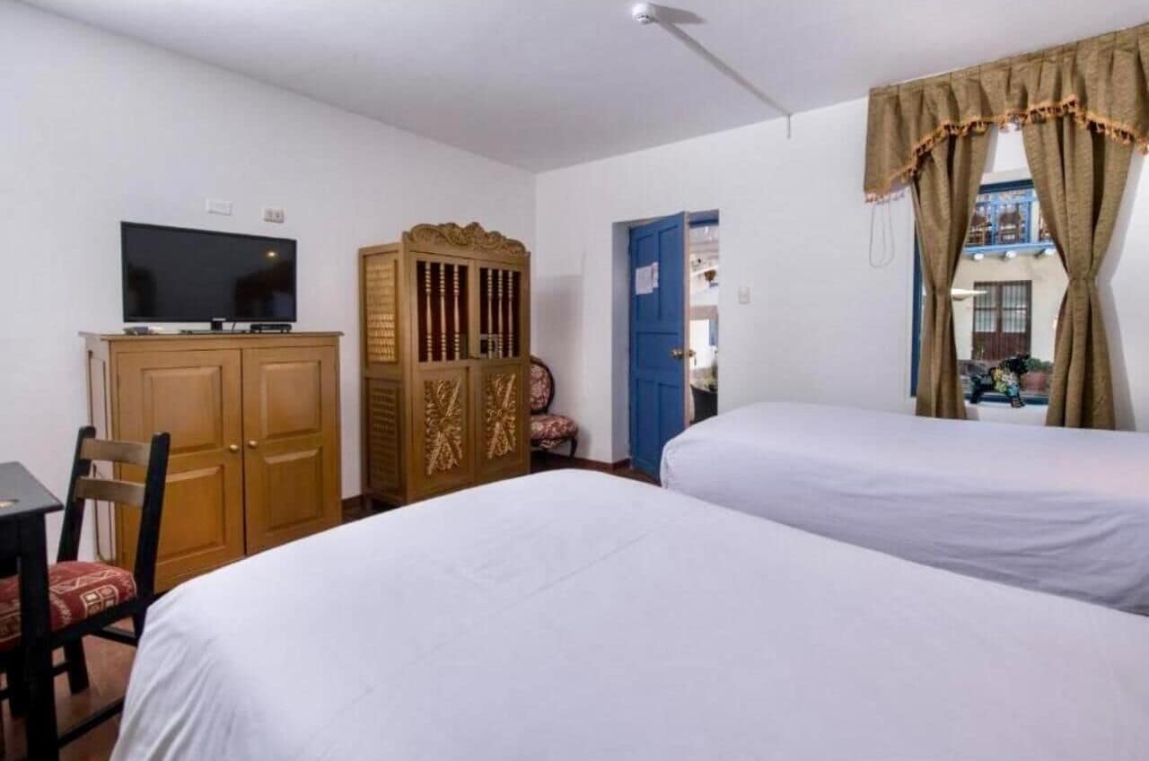 A room with two beds, a TV, a wooden cabinet, and a blue door.