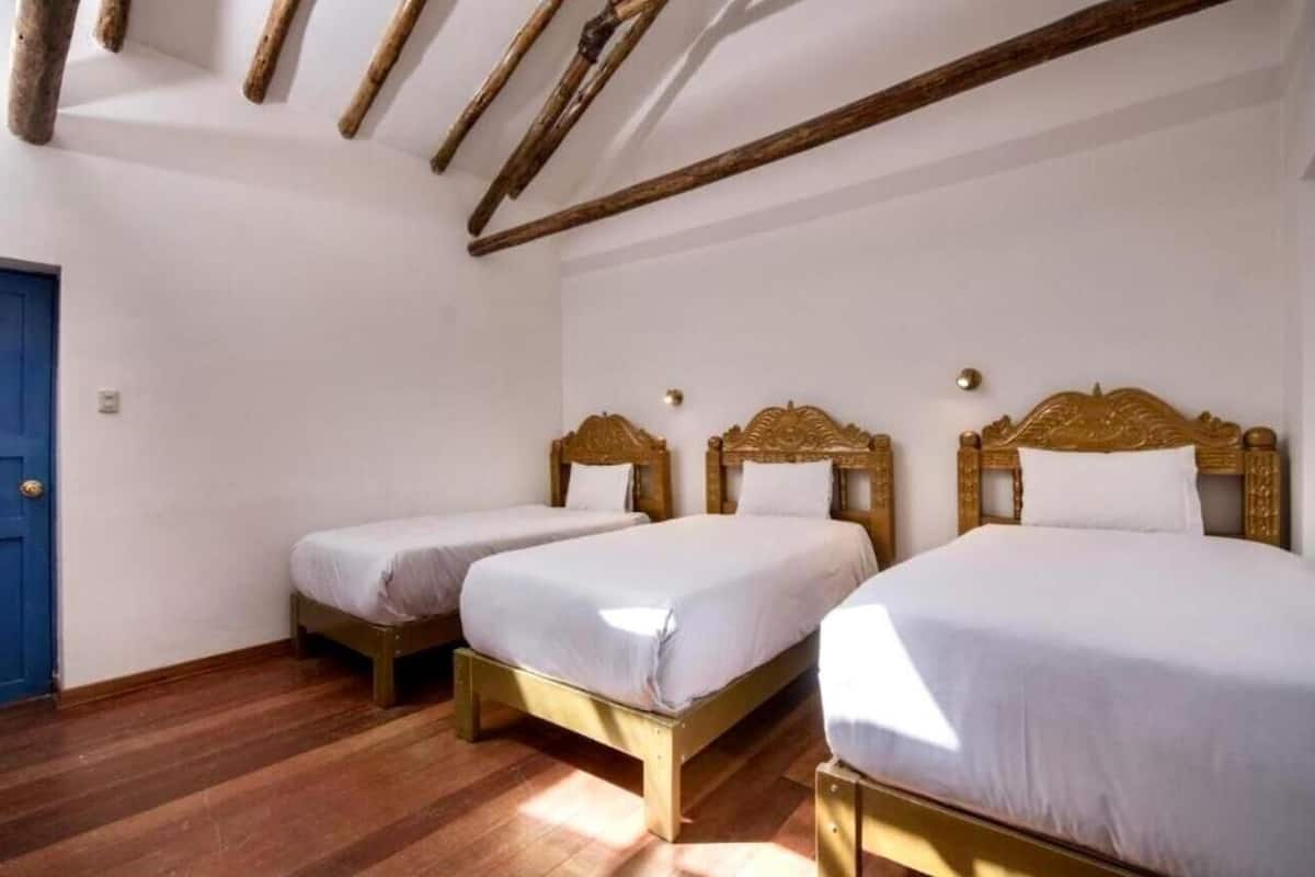 A room with three wooden beds with white bedding, a blue door, and exposed wooden beams on the ceiling.