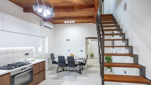 A modern kitchen with a dining area, wooden staircase, and a potted plant. - Nikos StoneHouse family home, located in the center of Prines (Rethymno)