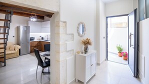 A modern kitchen with a refrigerator, microwave, and wooden cabinets. There is a dining area with a table and chairs, and a white cabinet with a mirror and decorative items. - Nikos StoneHouse family home, located in the center of Prines (Rethymno)