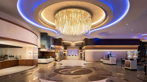 Un hall d’hôtel moderne avec un lustre central, un comptoir d’accueil et un grand écran numérique.