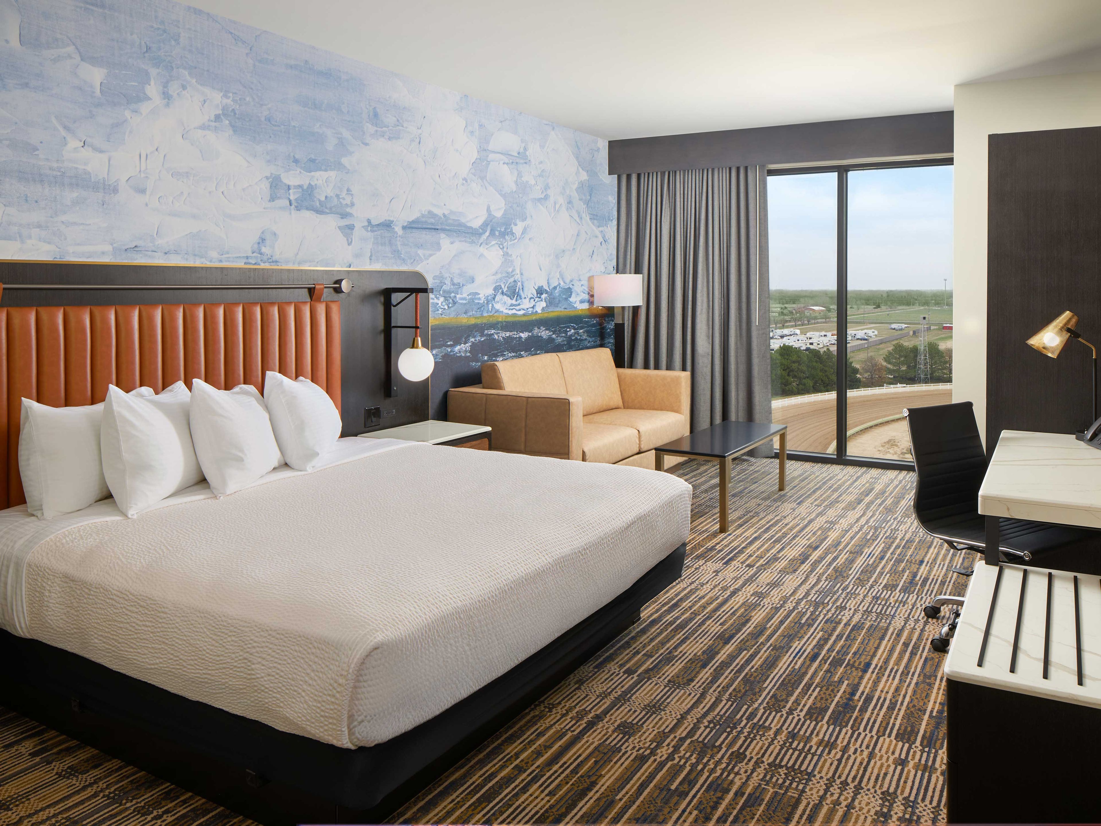 A hotel room with a large bed, a sofa, a desk, and a view of the landscape.