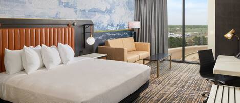 A hotel room with a large bed, a sofa, a desk, and a view of the landscape.
