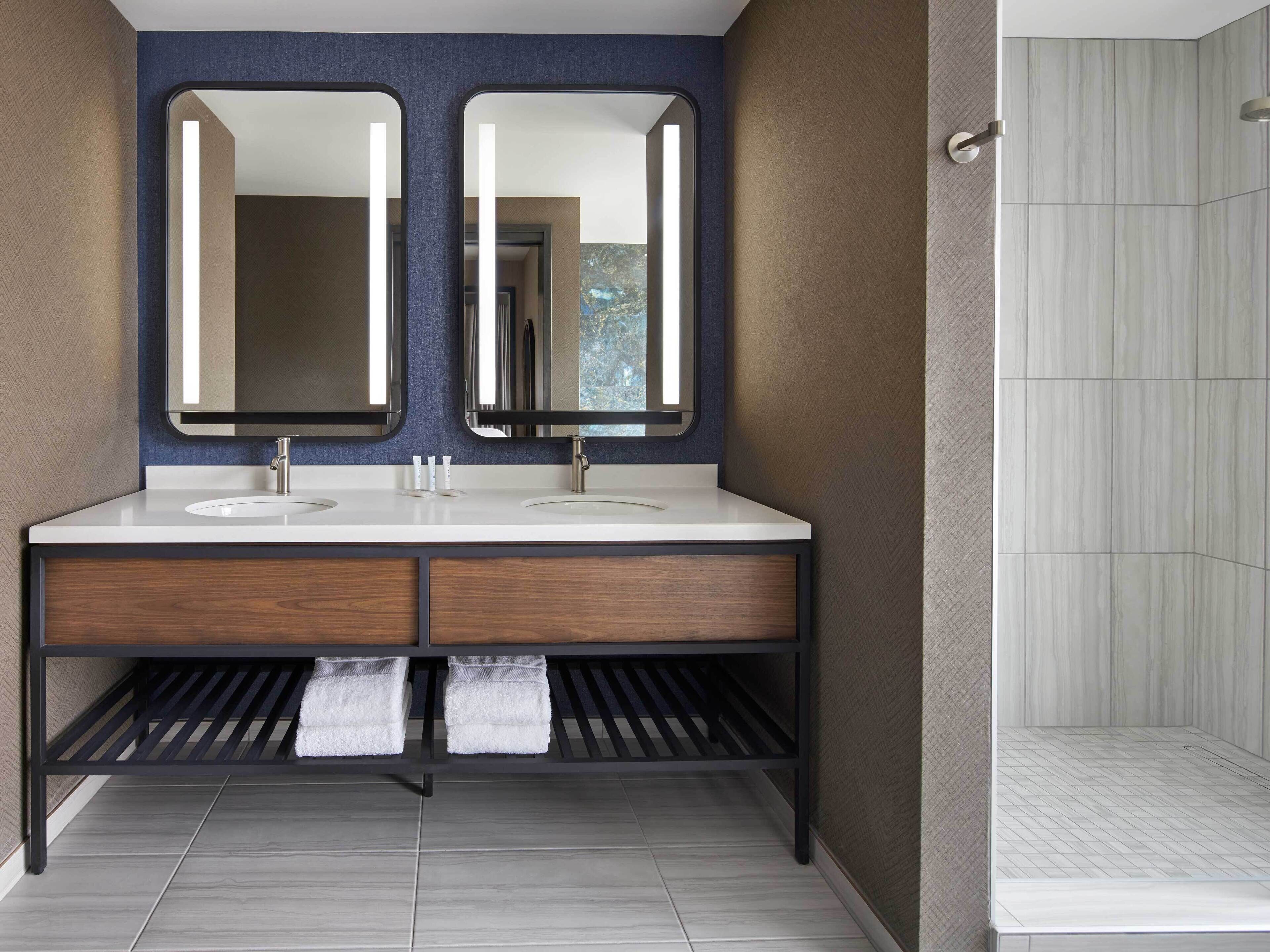 A modern bathroom with two sinks, a shower, and a large mirror.