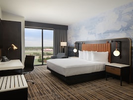 A hotel room with a large bed, a desk with a telephone, a chair, and a view of the outdoors.