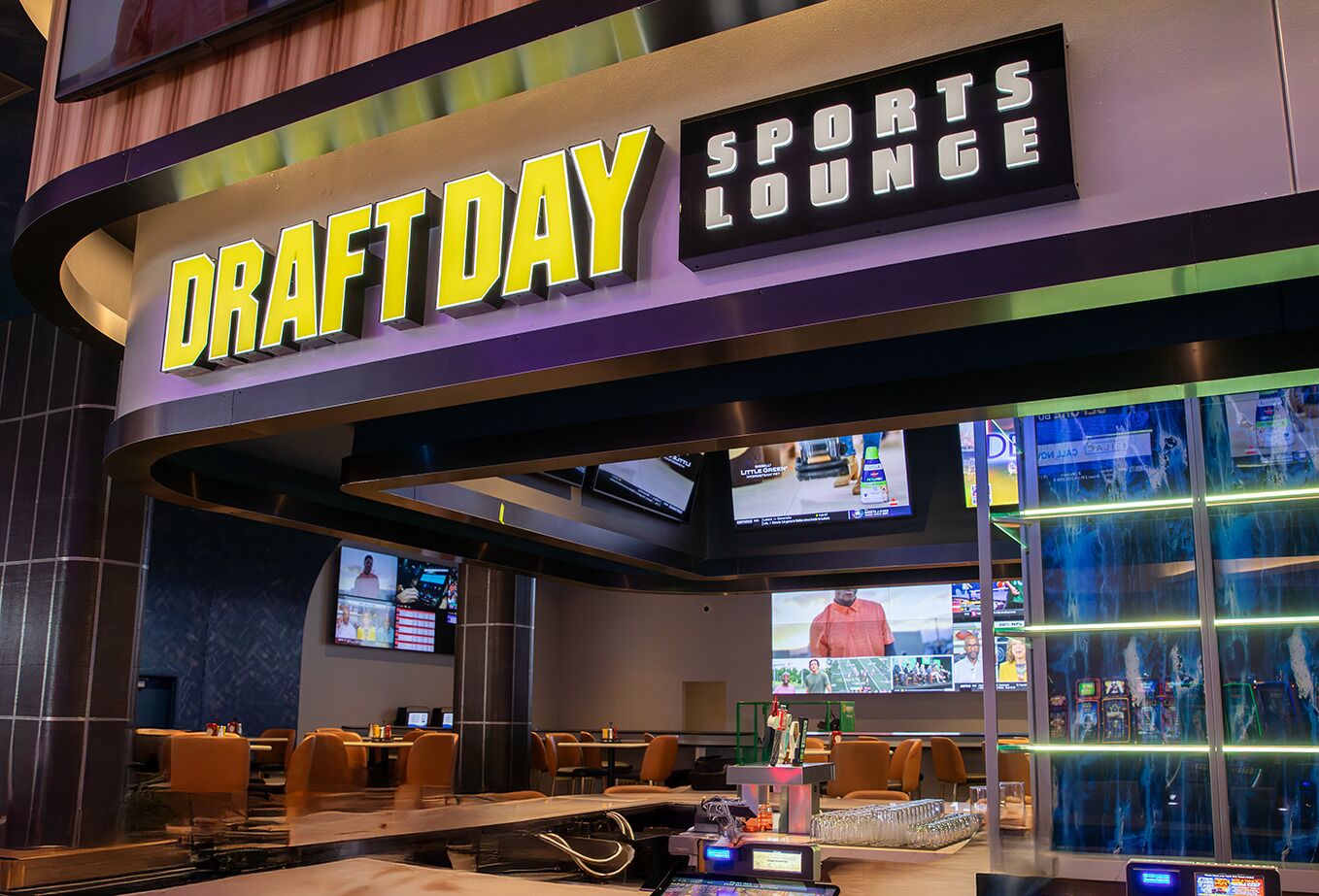 A sports lounge with multiple screens displaying sports content, comfortable seating, and a prominent 'Draft Day' sign.